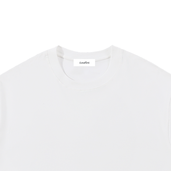 A white short-sleeve crewneck t-shirt with a small black 'Lovedfirst' logo printed on the lower right front, displayed flat against a solid white background.