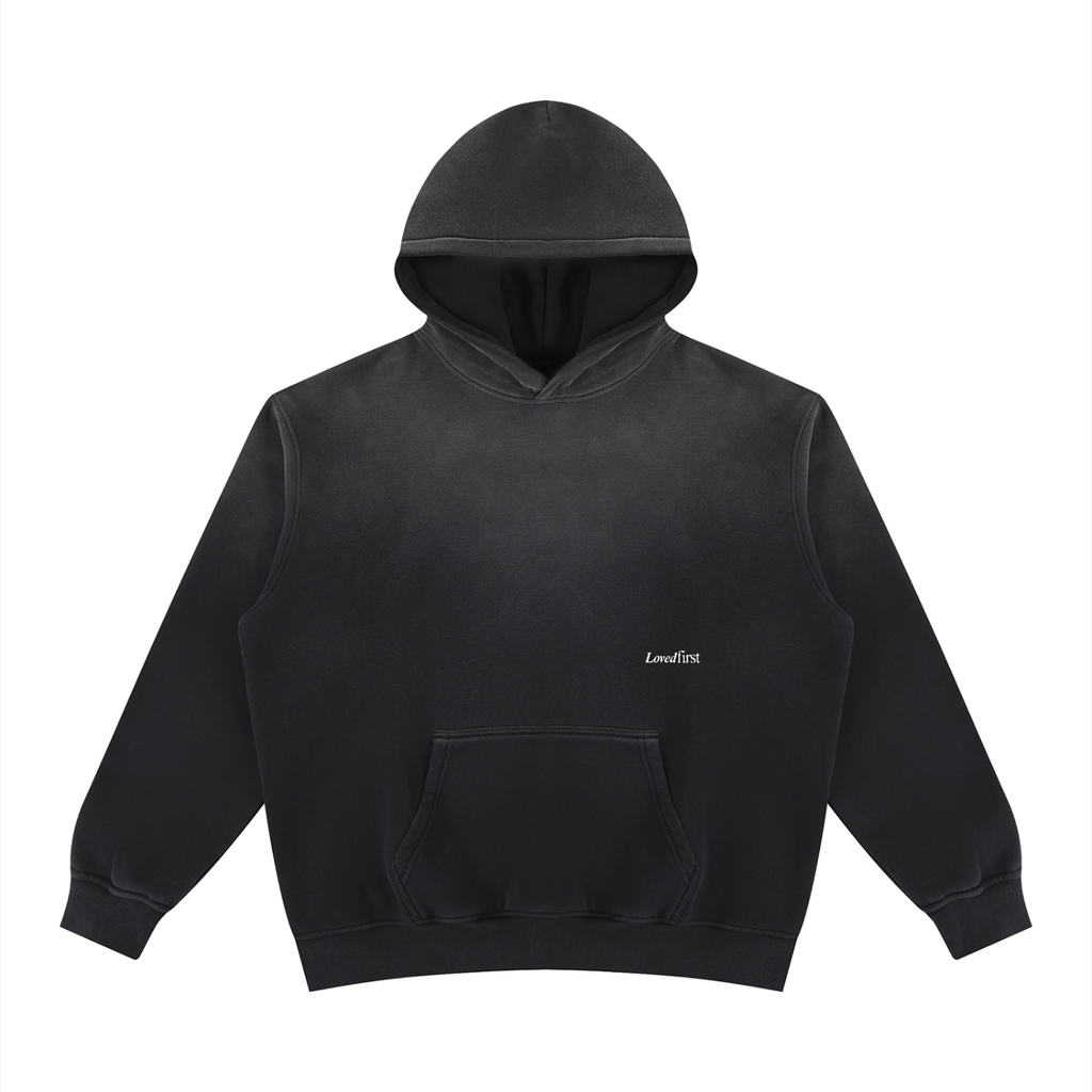 A black washed pullover hoodie with a small white 'LovedFirst' logo on the left chest, displayed against a solid white background.
