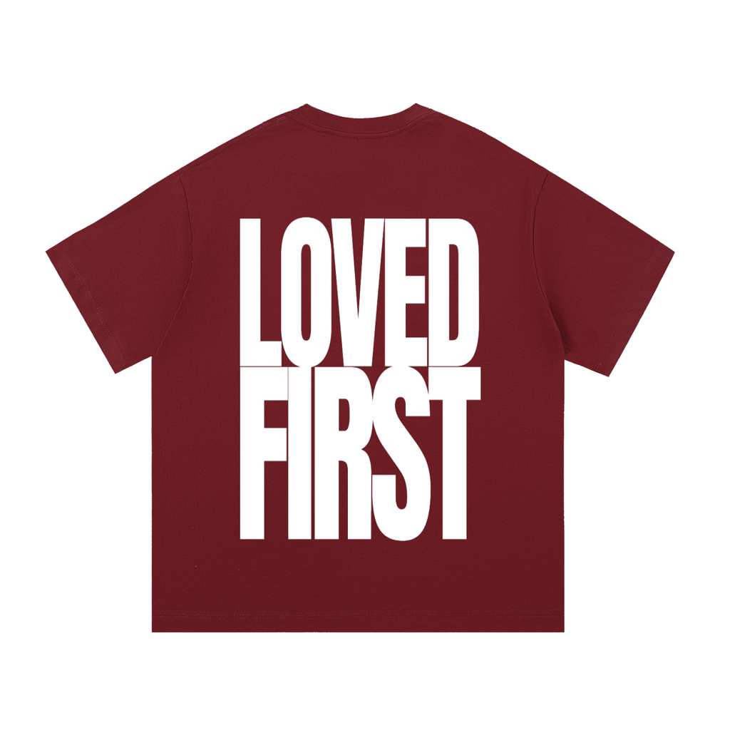 A Wine Red short-sleeve t-shirt with the words 'LOVED FIRST' printed in large, bold white block letters across the back, shown on a plain white background.