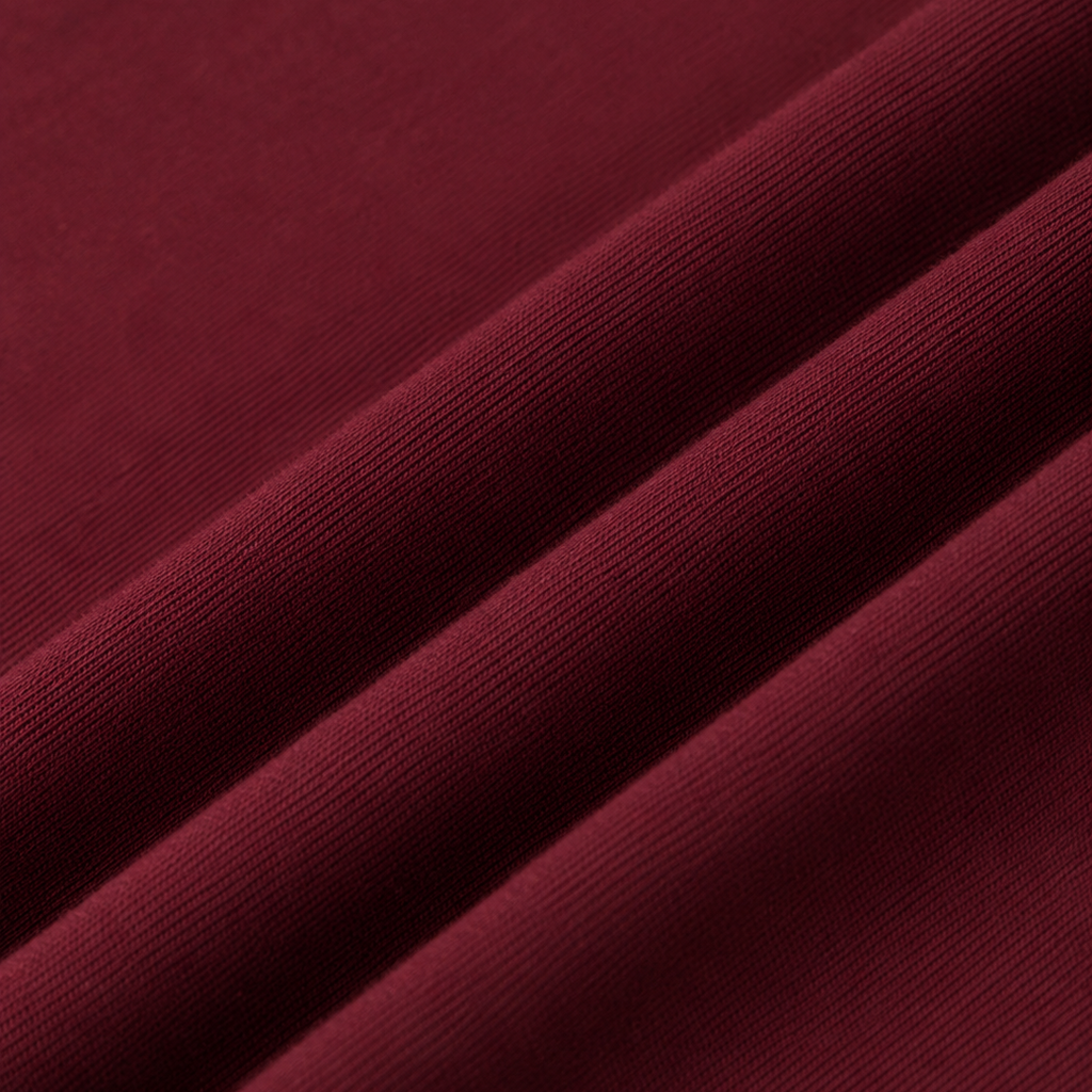 A close-up of draped wine red cotton tshirt fabric with a fine ribbed texture, showing soft folds and shadows.