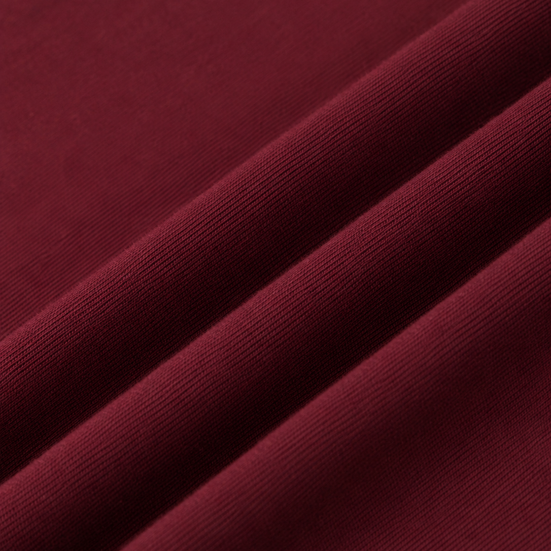 A close-up of draped wine red cotton tshirt fabric with a fine ribbed texture, showing soft folds and shadows.